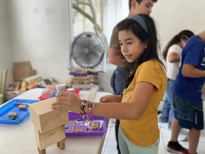 A learner building a wooden structure with real tools